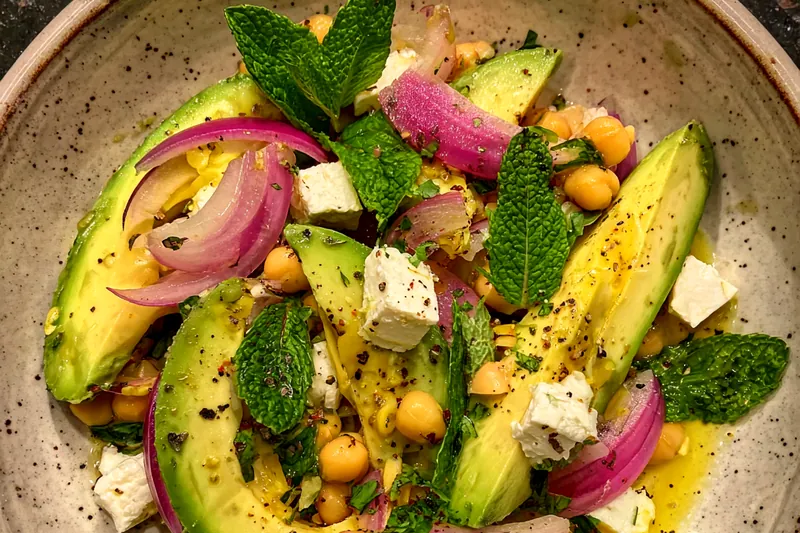 A chef tossing together the ingredients for Avocado Chickpea Salad Delight in a large bowl.
